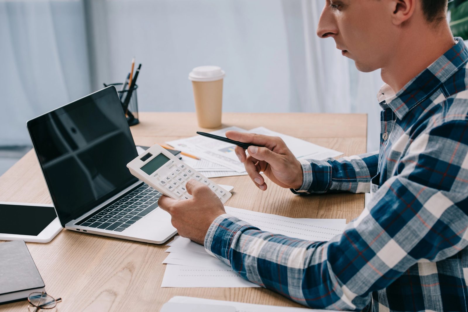 Tax professional reviewing figures with a calculator at a desk with a laptop and papers